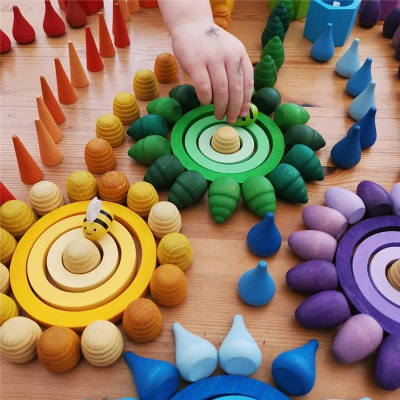 A hand places a wooden rainbow building block onto a circular arrangement of colored blocks.