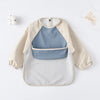 A light beige waterproof long-sleeved baby bib with a blue insert and white outer layer.