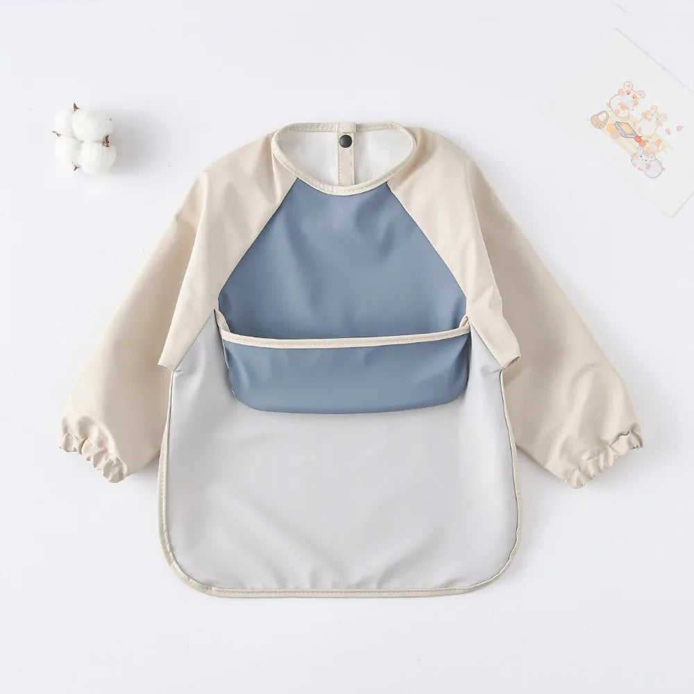 A light beige waterproof long-sleeved baby bib with a blue insert and white outer layer.