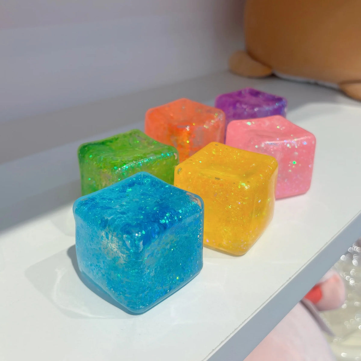 A collection of colorful square stress relief fidget toys in shades of green, orange, purple, and yellow are displayed on a w