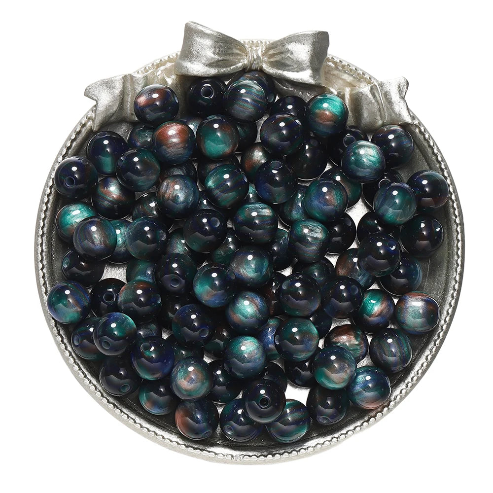 A collection of dark blue and green glitter cat eye resin beads in a silver-toned dish.