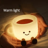 A hand holds a glowing coffee cup shaped night light emitting warm light.