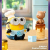 A yellow Minion figure wearing large glasses is sitting next to a brown bear collectible on a wooden table.