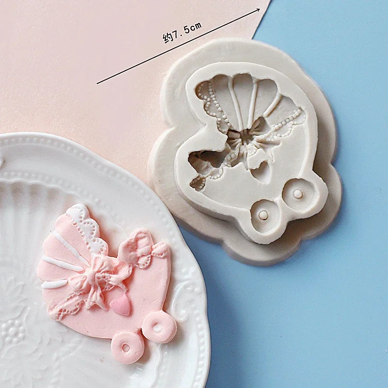 A set of silicone baby-themed cake molds including a stroller, bottle, and pacifier on a light pink background.