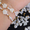 A hand is shown holding pearl bead jewelry featuring white floral and heart-shaped beads with gold accents.