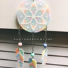 A circular ornament made of assorted colored fuse beads, hanging from a chain.