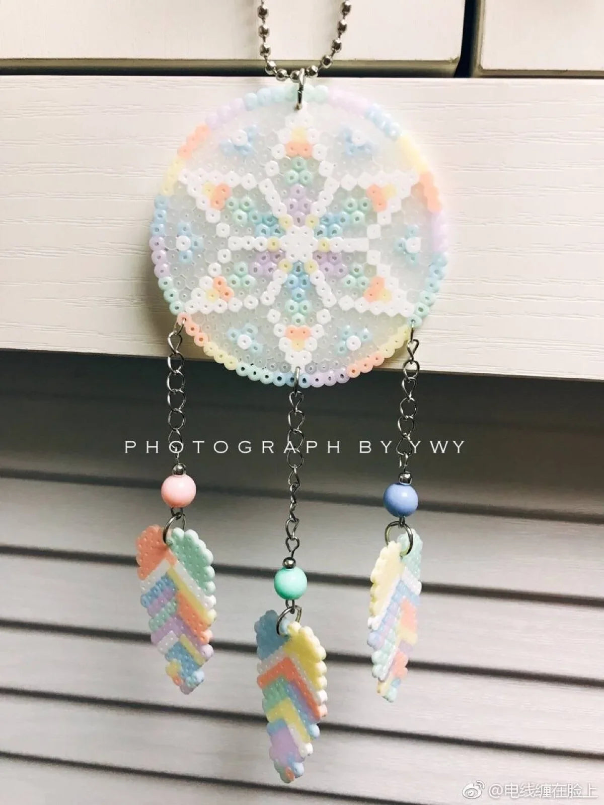 A circular ornament made of assorted colored fuse beads, hanging from a chain.