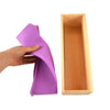 A hand holds a purple silicone soap mold with a cutting knife next to a wooden rectangular casing.