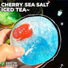 A hand squeezes a translucent blue sea salt iced tea squishy ball with a red fruit inside.