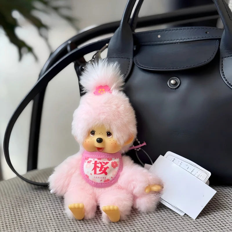 A pink fluffy cartoon plush toy with a face and a pink ribbon is resting on a gray surface next to a black leather handbag.