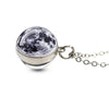 A silver pendant necklace featuring a round, dark celestial design with glowing white details.