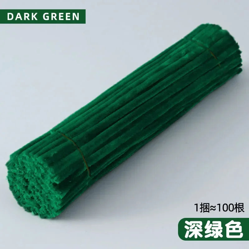 A dark green cylindrical craft material, likely chenille stems, is shown diagonally against a white background.