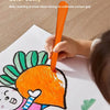 A child is using an orange crayon with a triangular grip to color a face on white paper.