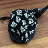 A black velvet face mask with white cat print patterns lying on a wooden surface.