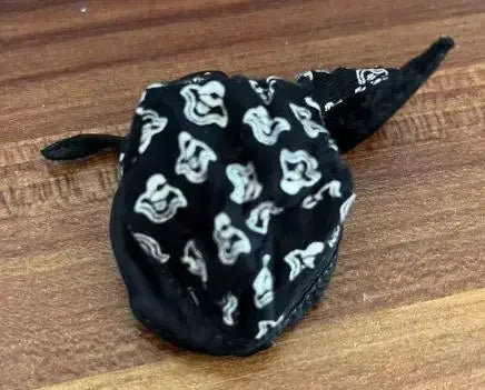 A black velvet face mask with white cat print patterns lying on a wooden surface.