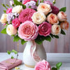 A vibrant bouquet of pink, peach, and purple roses and flowers arranged in a white vase.