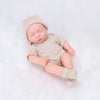 A realistic soft vinyl baby doll with a newborn outfit set lying on a white surface.