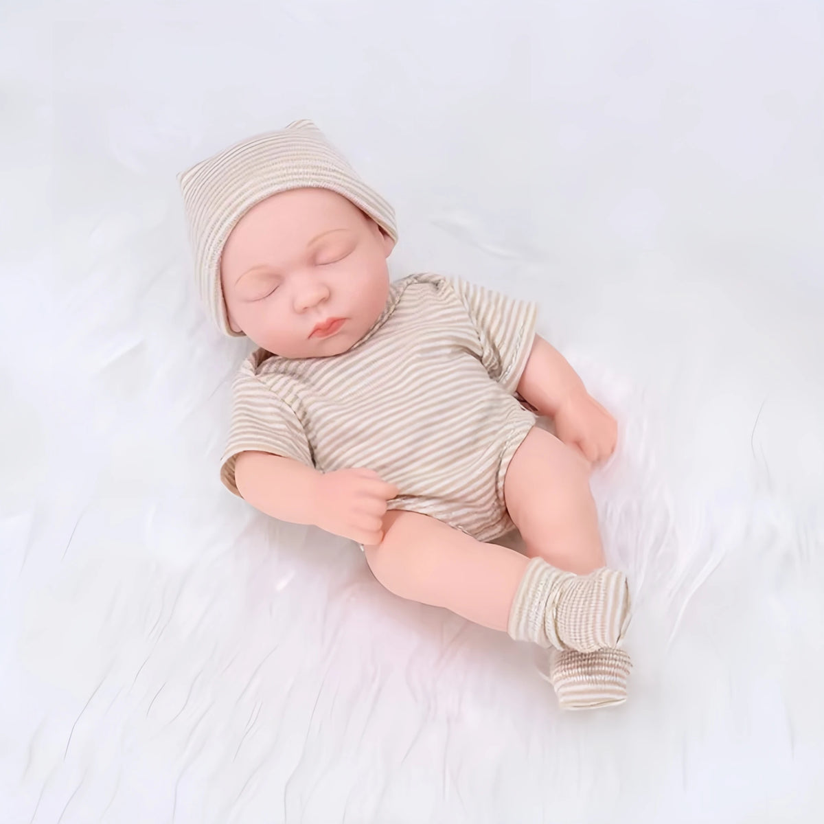 A realistic soft vinyl baby doll with a newborn outfit set lying on a white surface.