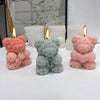 Three silicone candle molds shaped like teddy bears in pink and gray with lit candles.