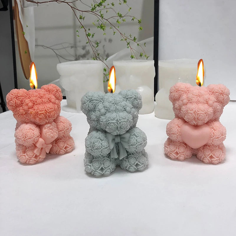 Three silicone candle molds shaped like pink and blue teddy bears with lit candles on a white surface.