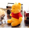 A yellow Winnie the Pooh plush bear wearing a red shirt sitting on a wooden surface next to an old radio.