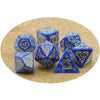 A set of blue and gold dragon-inspired polyhedral dice including a d10, d12, and tetrahedron, displayed on a gold glitter bac
