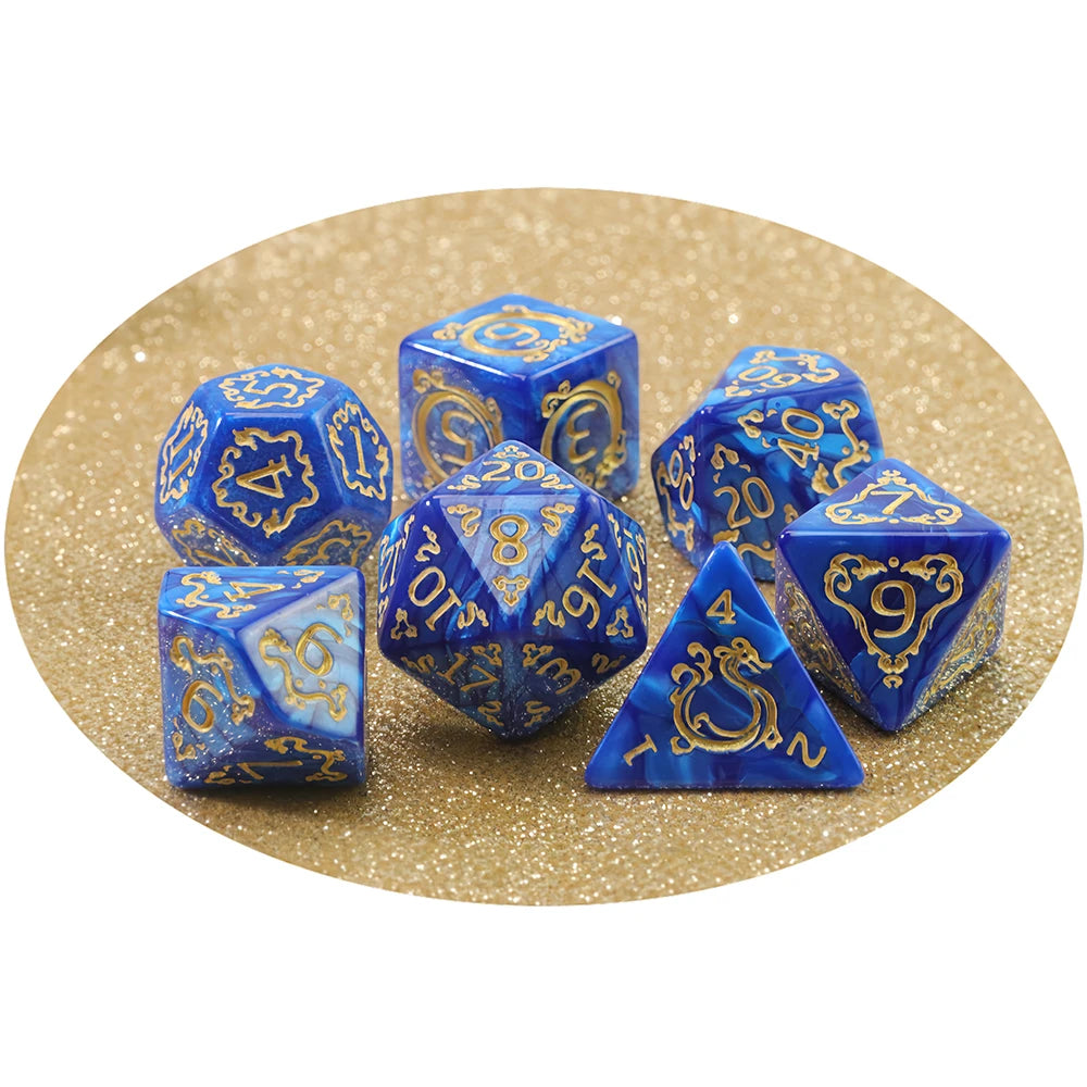 A set of blue and gold dragon-inspired polyhedral dice including a d10, d12, and tetrahedron, displayed on a gold glitter bac