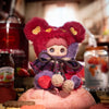 A plush charm of a tiny bear cookie with fluffy red and purple fur and a dark bow.