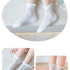 A pair of white floral cotton kids socks worn on a foot, displayed next to a pair of shoes.