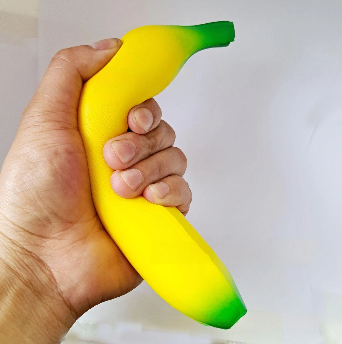A hand is holding a yellow squishy banana stress relief toy with green accents.