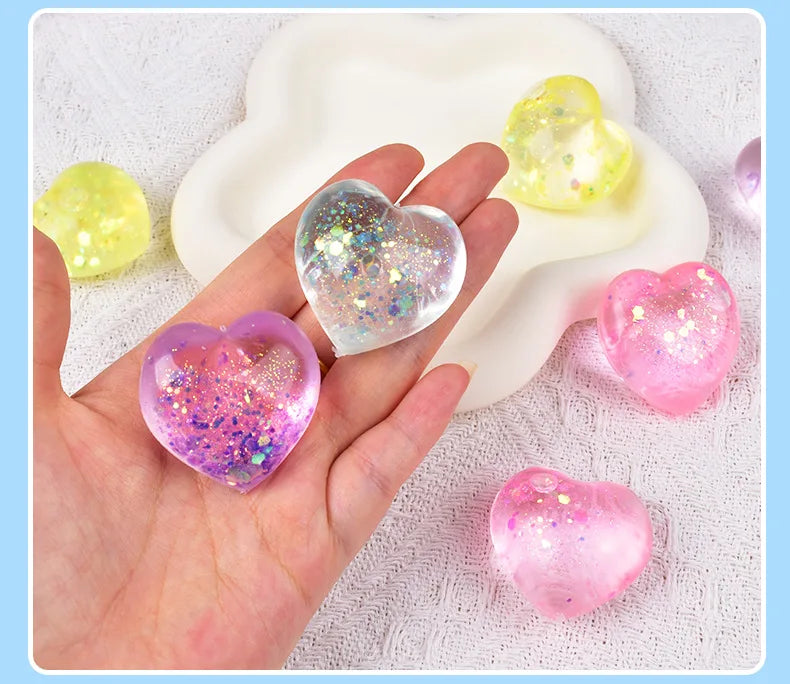 A hand holds several iridescent heart-shaped squishy toys in shades of yellow, pink, and purple foam.