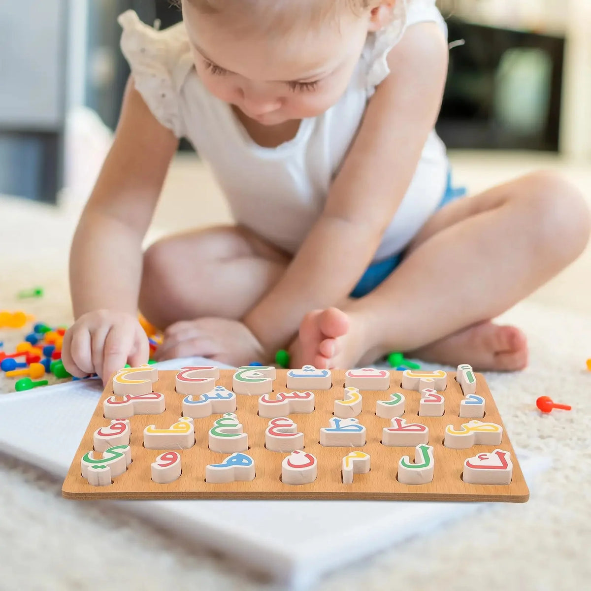 A young child is playing with a wooden puzzle set of the Arabic alphabet letters on a white surface.