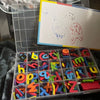 A clear plastic box filled with colorful magnetic letters for educational learning.