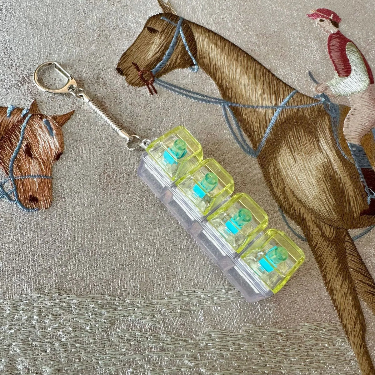 A brown horse figurine is shown with a clear acrylic keycap fidget keychain attached to its bridle.