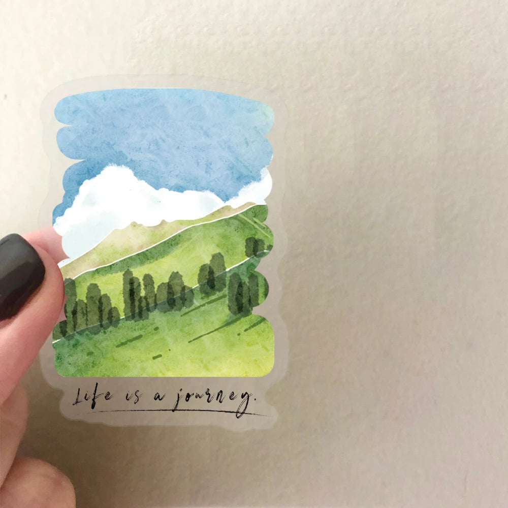 A watercolor sticker depicting a green rolling hill landscape under a blue sky with white clouds.