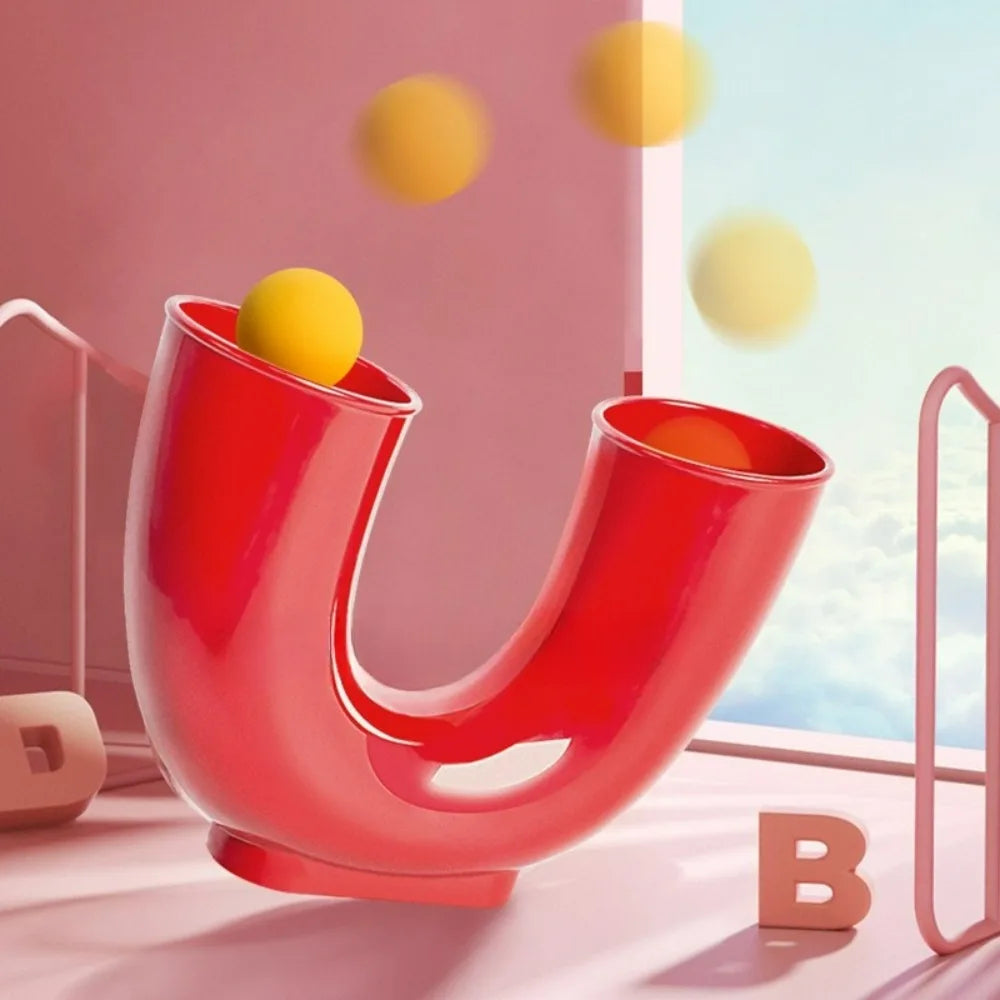 A bright red U-shaped toy for juggling balls with yellow spheres, shown in a studio setting.