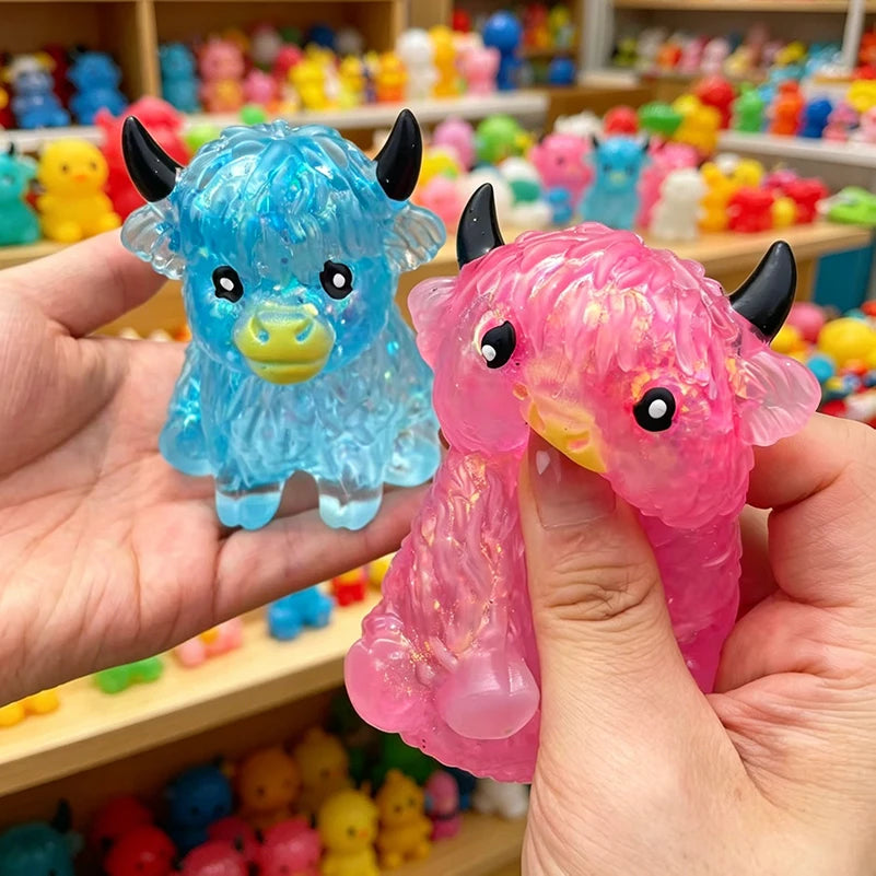 A hand holds a bright blue glitter highland cow squishy stress relief fidget toy.