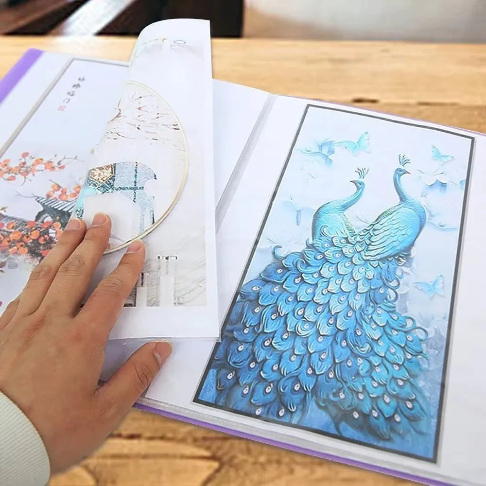 A hand is holding an open transparent diamond painting storage album displaying a detailed blue bird design.