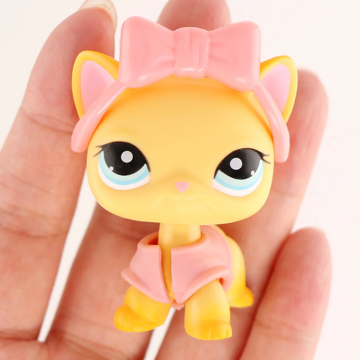A small yellow cat figure with pink ears and a pink bow is held in a person's hand.