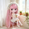 A pink Blyth fashion doll with long hair and a white floral crown sitting on a white stool near a window.