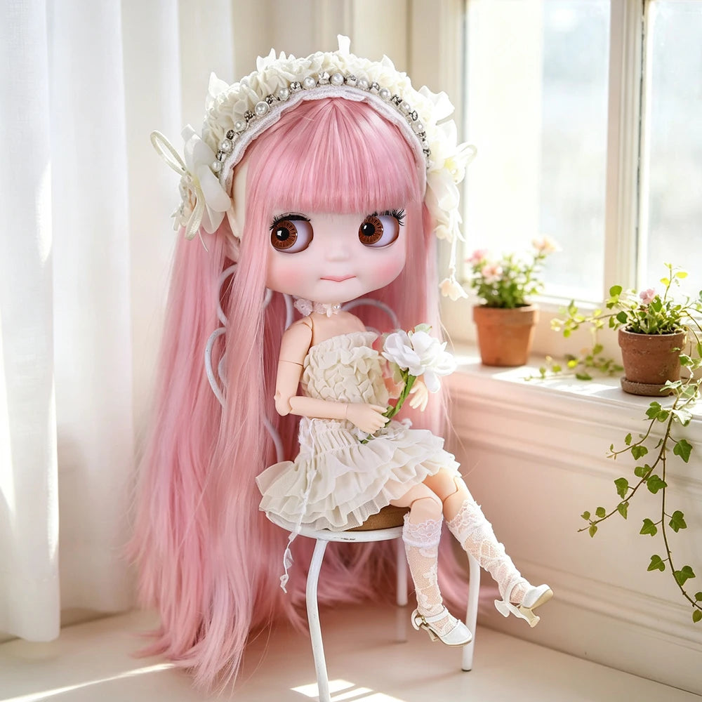 A pink Blyth fashion doll with long hair and a white floral crown sitting on a white stool near a window.