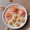 A bowl of light pink rose petals and small flower forms arranged on a neutral background.