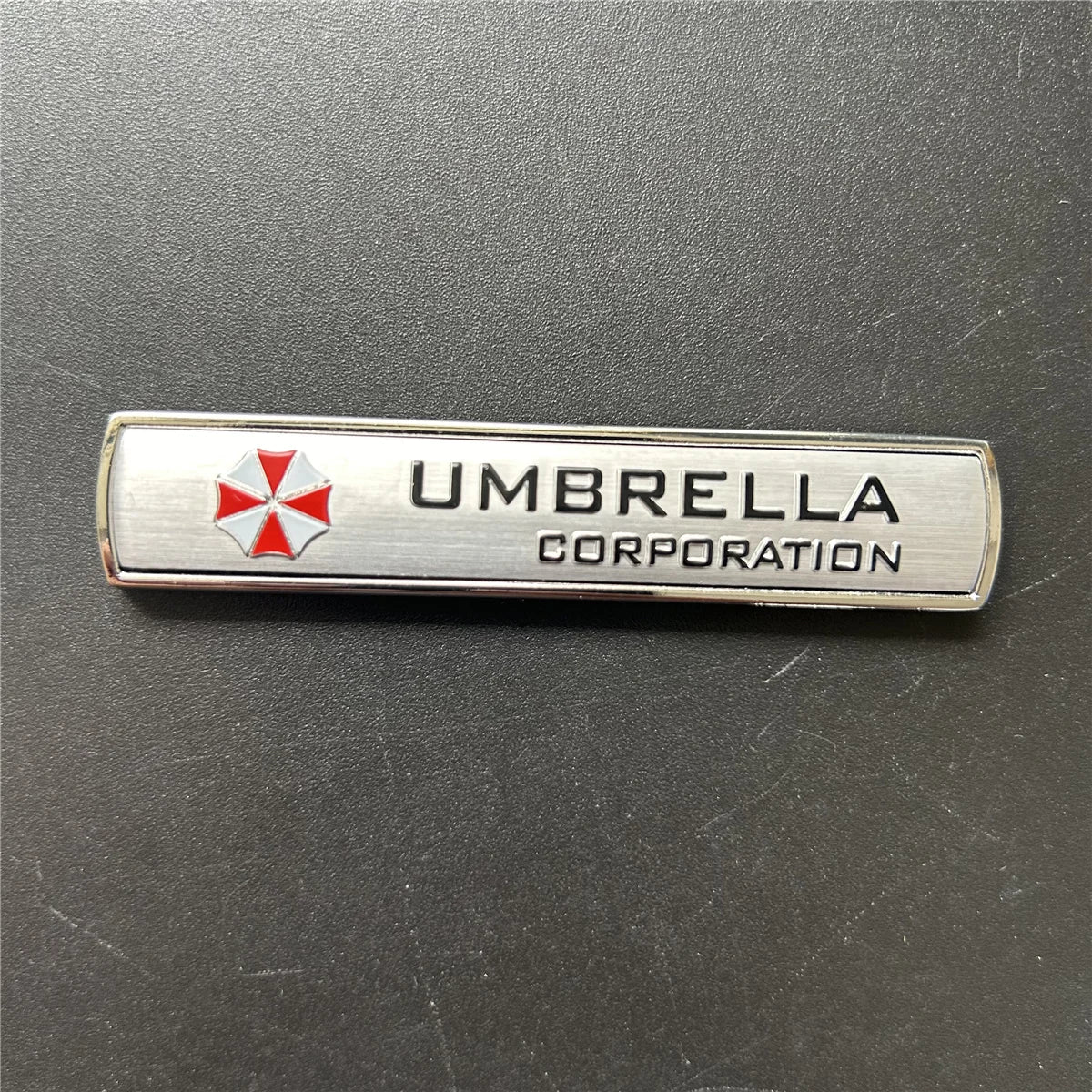 Silver metal badge with an umbrella emblem and the text UMBRELLA CORPORATION