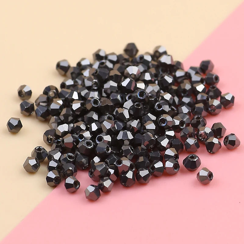A pile of small, dark black electroplated crystal glass beads for jewelry making on a pink and beige surface.