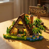 A wooden miniature building set depicting a cabin and windmill scene with plants and a sign.