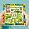 A hand holds a magnetic color and number maze board featuring dinosaurs and numbered paths.