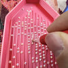 A close-up view of a pink diamond painting tray with numerous small clear beads arranged in rows.