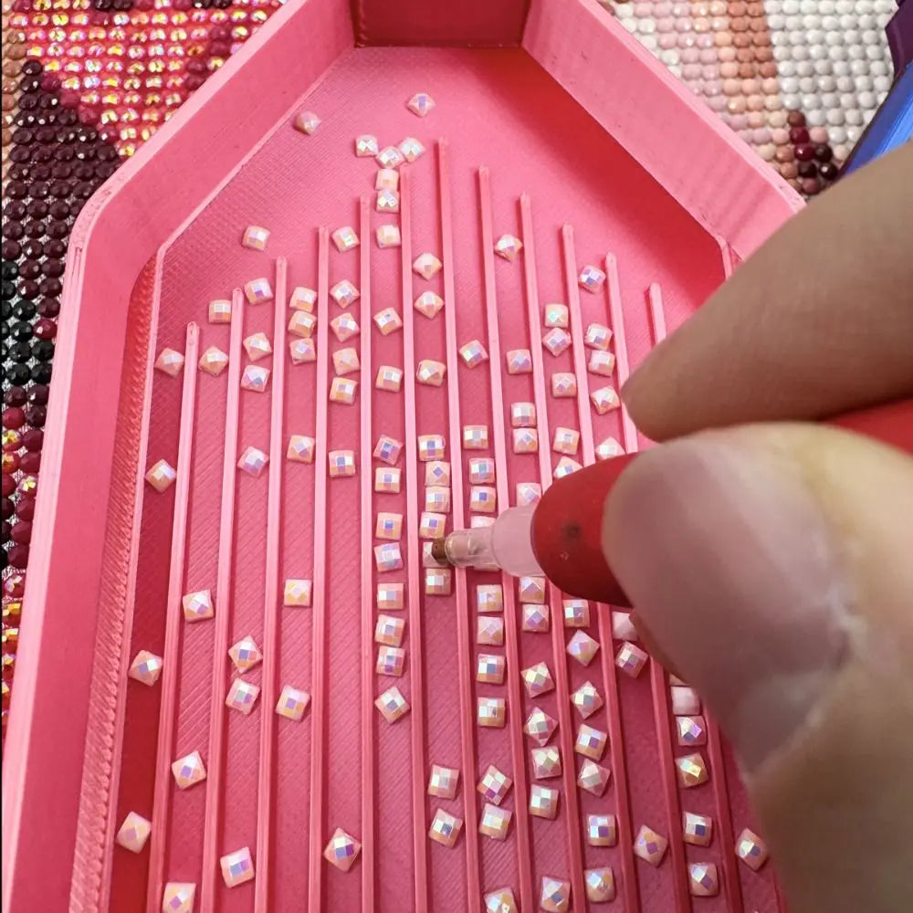 A close-up view of a pink diamond painting tray with numerous small clear beads arranged in rows.