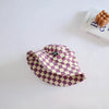 A purple and cream checkered bucket hat is displayed on a white surface next to a book.