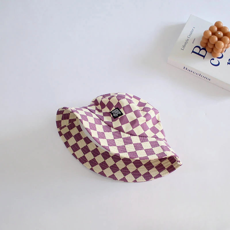 A purple and cream checkered bucket hat is displayed on a white surface next to a book.
